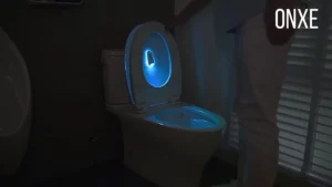 Motion-activated toilet bowl night light glowing soft blue inside a darkened bathroom at night